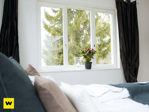 Helles Schlafzimmer mit großem Fenster, Vorhängen und Blumentopf auf der Fensterbank.