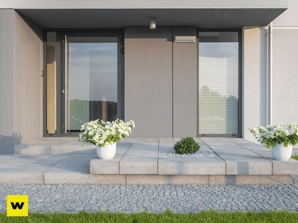 Moderner Hauseingang mit grauen Fliesen, zwei weißen Blumentöpfen und Glasfront.